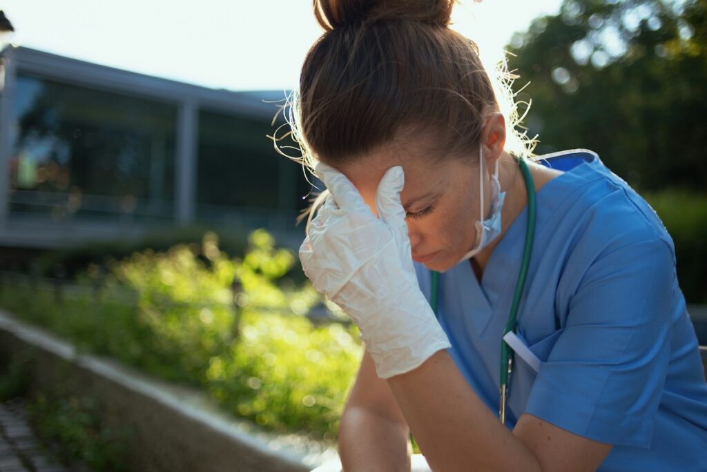 A woman nurse experiencing nurse burnout with her hand on her forehead.